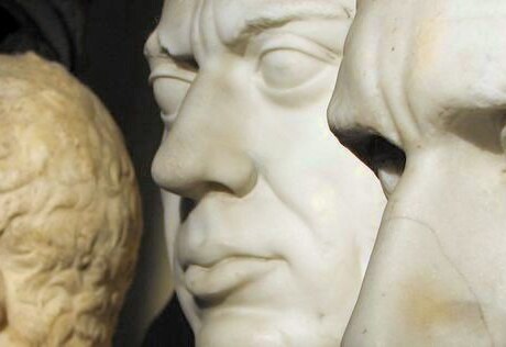 Two marble faces of men in the foreground. There is another statue in the background.
