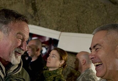 Robin Williams and another man are inside a military base. Robin is saying something to the officer and making him laugh.