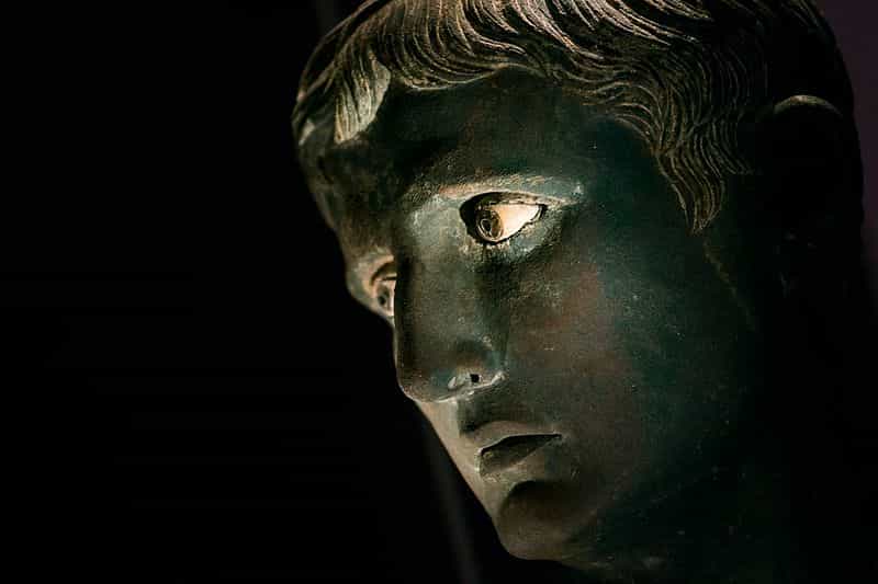 A bronze head with inlaid eyes. The eyes are blue. The face is longish. Octavian's features are there: his mop of hair, his long neck, his long nose curved to one side, his small mouth, the high cheekbones, the protruding ears.