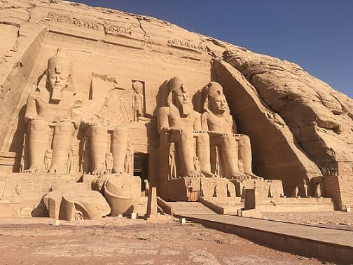 Massive rock temples with colossal sculptures in front.