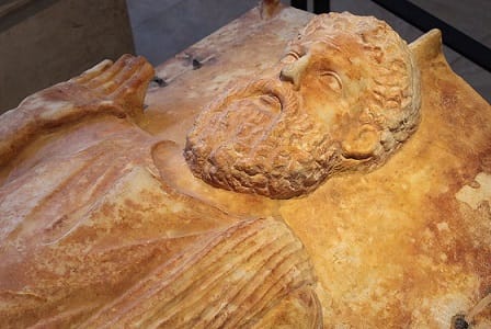 A sarcophagus with the face and body of a man sculpted on top.