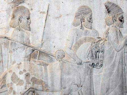 A bas-relief. A procession of men walk next to two small horses. The horse's head are at the same level as the men's shoulders.