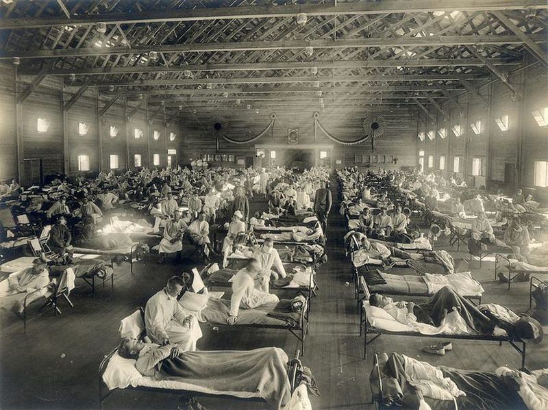Inside a large warehouse which is filled with rows of beds. A sick soldier lies on each bed.
