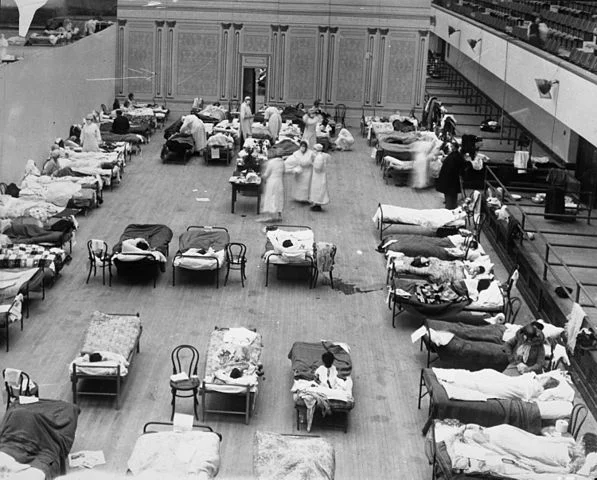 A large room with impromptu beds set up everywhere. Each bed has a patient, and nurses are attending them.