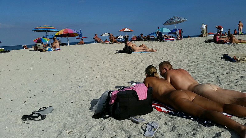 Picture of a nudist beach with white sand and many nudists.