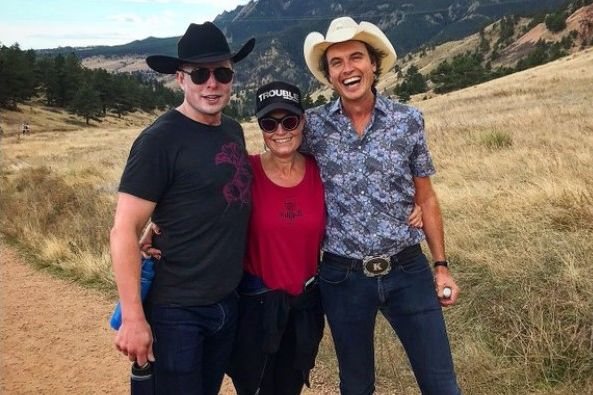 A recent picture of the Musk siblings in an arid landscape. The three stand posing for the camera, hugging and smiling. Elon is on the left, his sister in the middle, and their brother on the right.