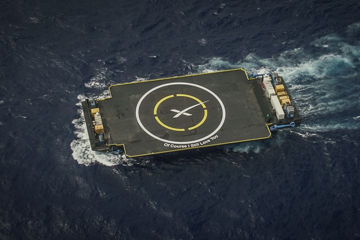 Picture of another landing pad floating in the middle of the ocean. This one says, in big letters than can be seen from the sky: "Of course I still love you."
