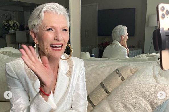 Another picture of Maye Musk. In this one she is also impeccably and modernly dressed. She wears big hoop earrings and is laughing.