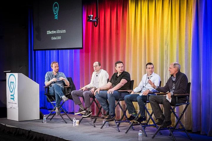 Five people sitting and talking on stage. One is the interviewer and the other four are panelists.