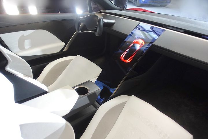 The interior of a car. It has very simple lines, the dashboard has no buttons or gadgets, only one black computer screen between the driver and the passenger's seat.