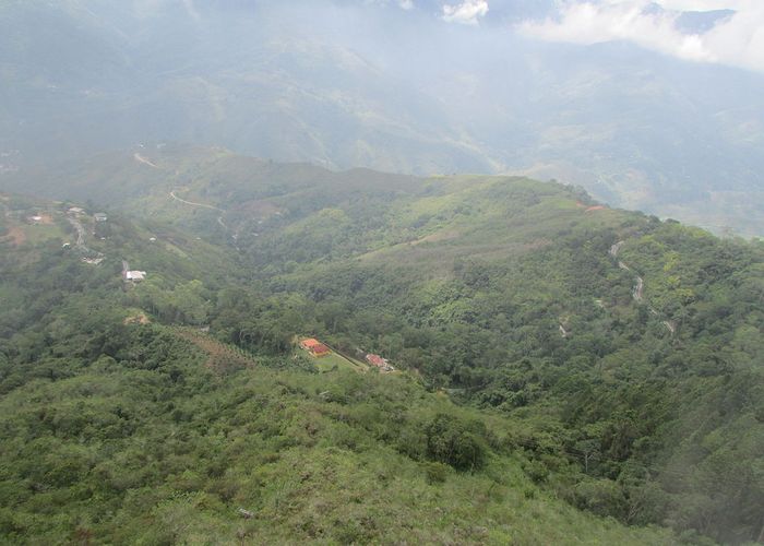 Aerial view of a mountain range covered in vegetation. There are big mountains and a two or three houses spread on the top.