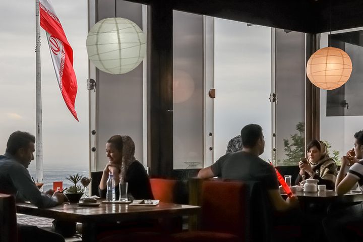 Modern, chic restaurant with big glass windows. Men and women sit at the tables chatting.