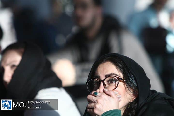 A woman watches a soccer match inside a mall. She covers her mouth with both hands in disbelief.