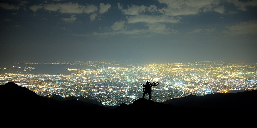 Panoramic view. Picture of Tehran viewed from a mountain, at night. On the mountain one can see the silhouette of a cyclist watching the lights of the large city below.