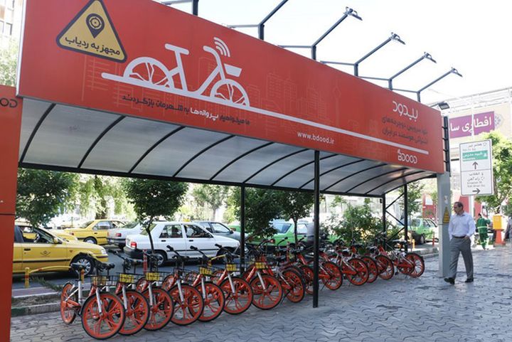 A stand with a row of red bicycles parked in the middle of the city.