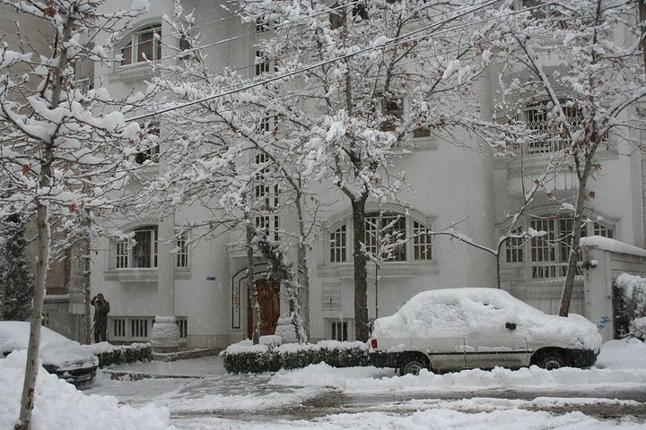 An elegant townhouse with a car parked outside. The car, a tree, and the street are covered in several centimetres/inches of snow.