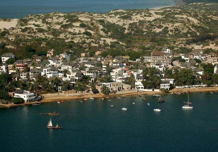 Aerial shot of an island with white houses along the shore. The sea is deep blue.