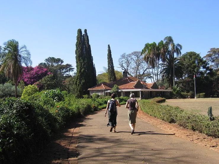 Two women walk on a road towards the same house. The house seats on large grounds. There is only nature around.