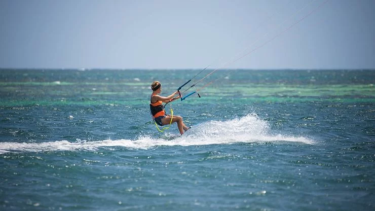 Bright clear, sunny day in the ocean. A woman is kiteboarding (riding a board on the sea while holding a kite that pulls her)