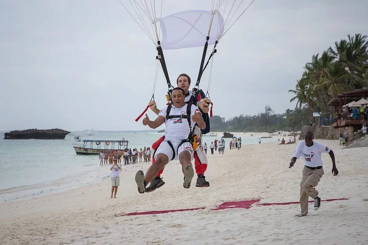 Two men strapped to a parachute land on the beach.