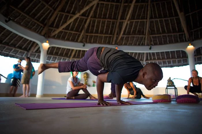 A man practices an arm balance while other yogis watch him.