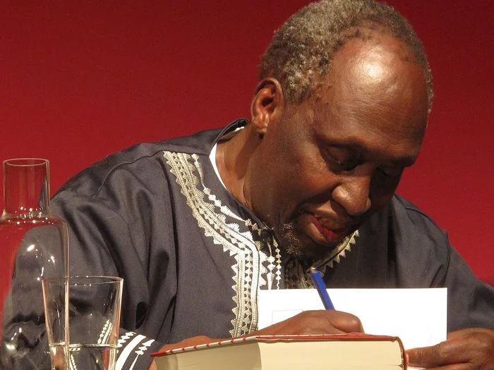 A man dressed in traditional African clothes signs a book.