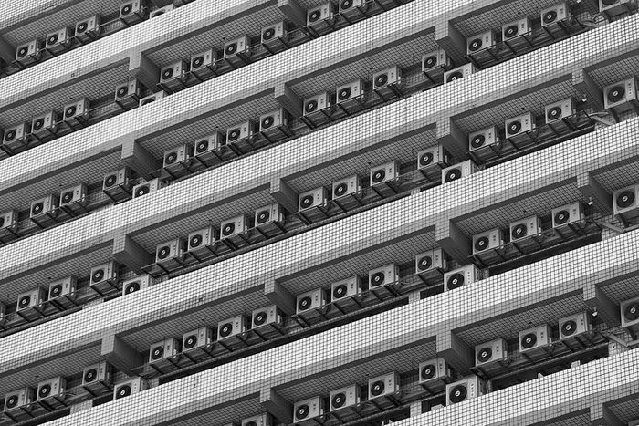Picture of the facade of a modern building. It has a row of air conditioners on each floor.