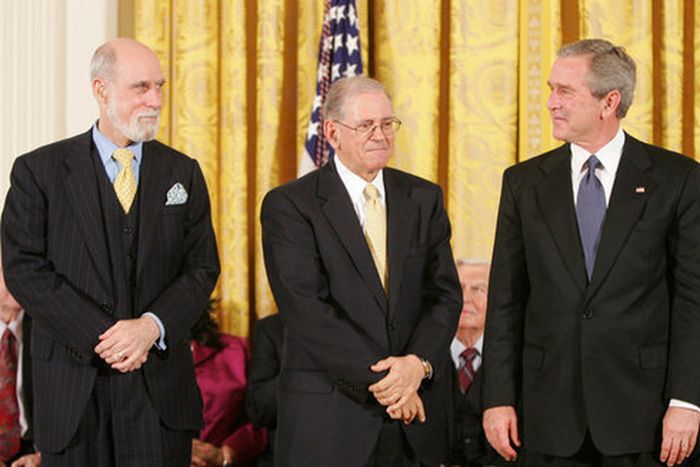 Two men in their sixties pose for an official portrait with President Bush. All three wear black suits.