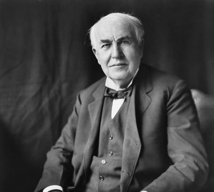 Black and white photo of Thomas Edison. He sits down, wears a suit, and is about sixty years old.