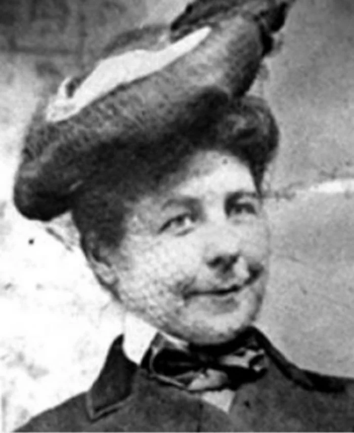 Old black and white picture of a youngish woman, perhaps in her thirties. She wears a hat and a high-collared shirt.