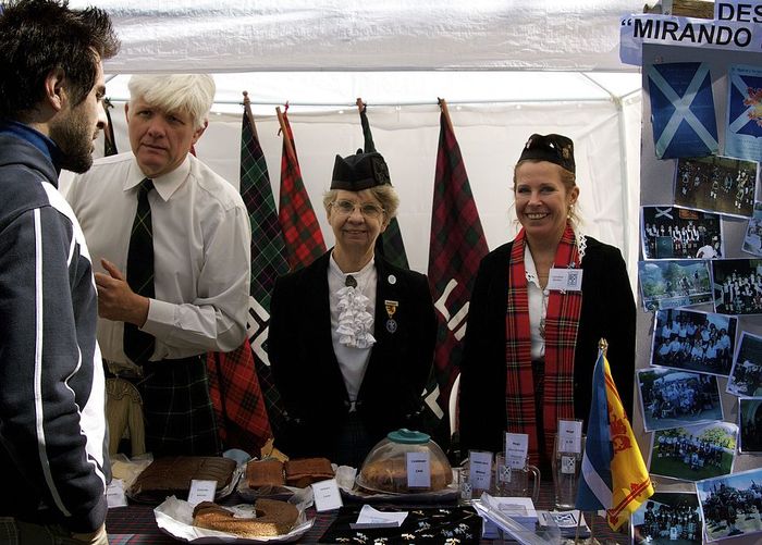 A man and two women dressed in Scottish traditional clothes at a fair.