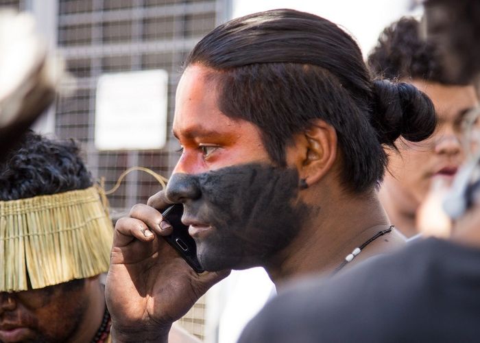 A young man with half his face painted in black speaks on his cell phone.