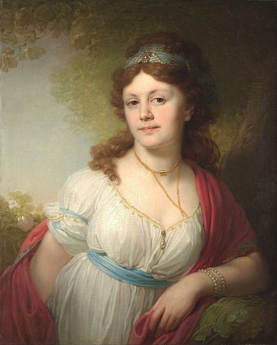 A teenage woman. She has long, brown, hair, a square face, and is dressed in white.