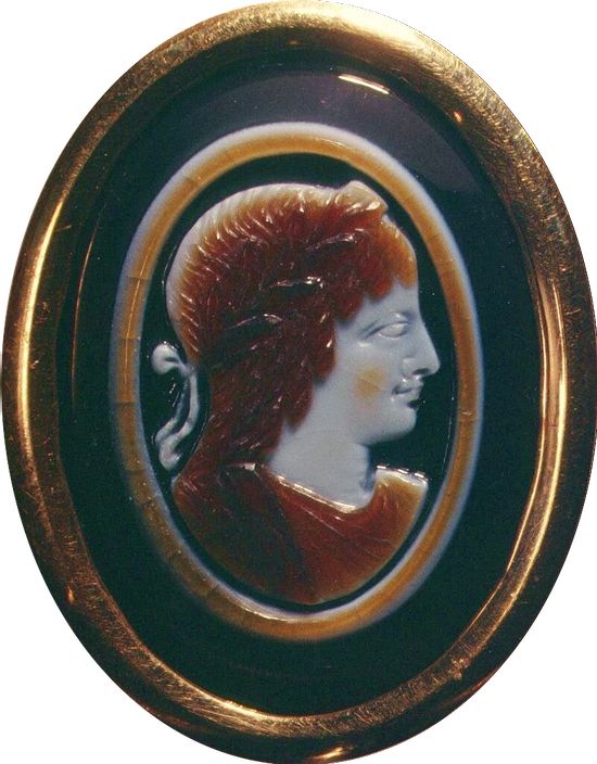 A white and brown cameo. Profile of a woman. Her face is in white. Her hair and clothes in brown. She has a standard Greek profile. Small forehead, long nose, thick lips, prominent chin. She wears a diadem.
