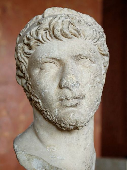 Marble face of a youngish man. His face is oval and full. He has wavy hair and a small forehead. His nose is smallish and broad, his lips are thick, his chin prominent and round.
