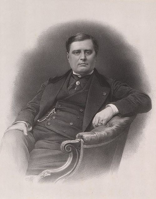 Black and white photograph. A man, probably in his fifties. He seems powerful. He is wearing an elegant black suit and is sitting down, looking directly at the camera. His face is squared and his hair seems dark. He looks a lot like Napoleon.